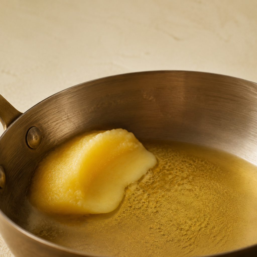 Solid ghee melting into clear gold in a steel pan